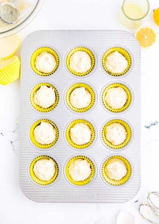 cupcake batter are filled inside yellow cupcake liners on a metal muffin pan