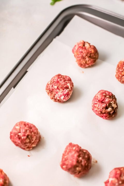 ground beef rolled into meatballs on a baking sheet lined with parchment paper