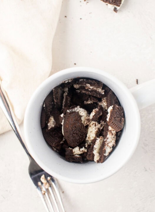 crushed oreo cookies in a white mug next to a metal fork