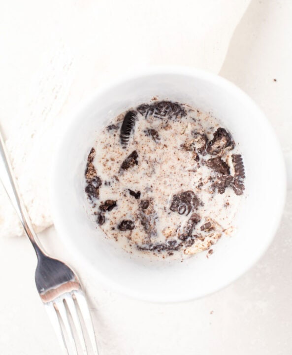 crushed oreo cookies in a mug with whole milk next to a metal fork