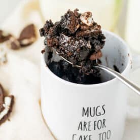 oreo mug cake on a metal spoon in a white mug that says "mugs are for cake, too"