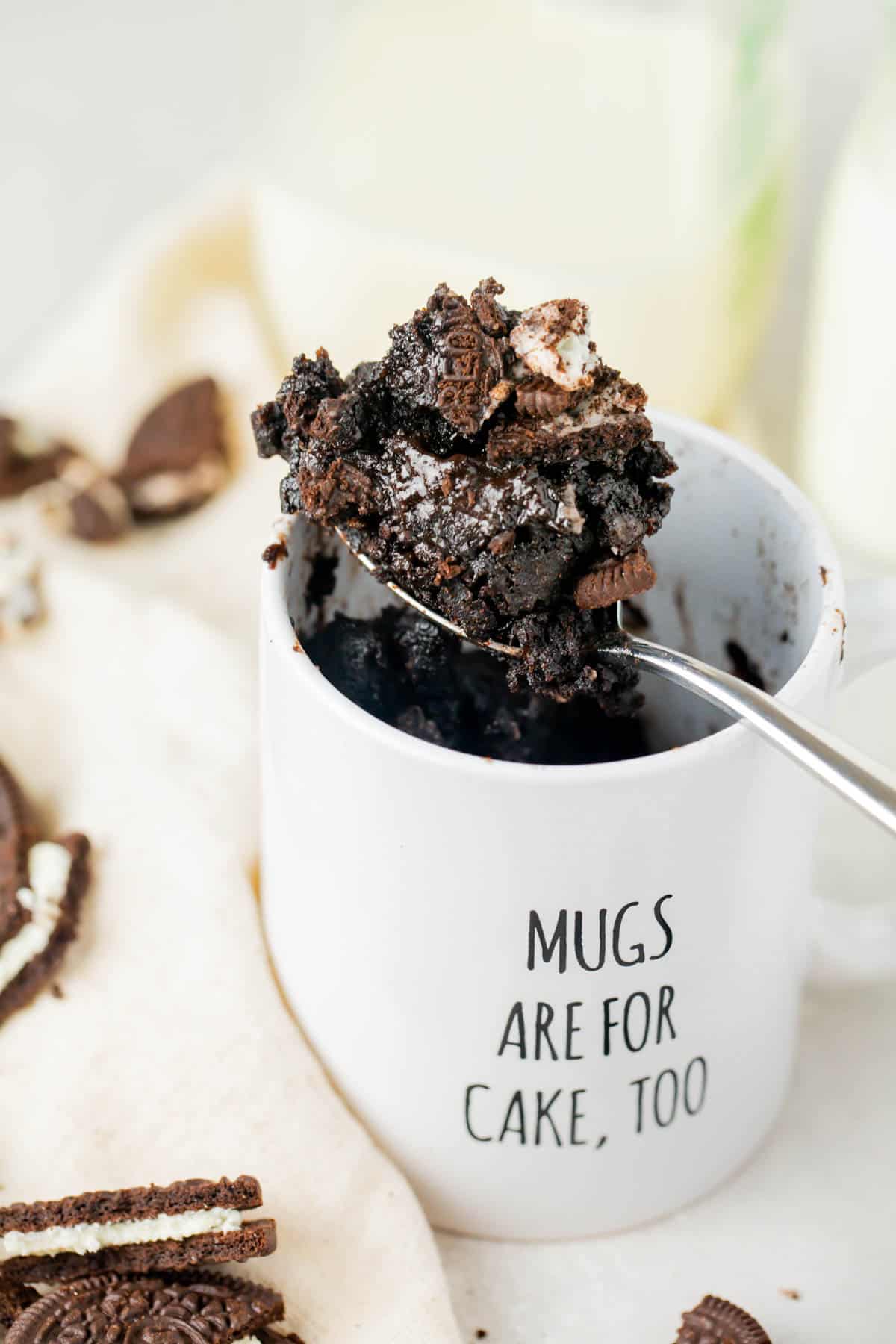 oreo mug cake on a metal spoon in a white mug that says "mugs are for cake, too"