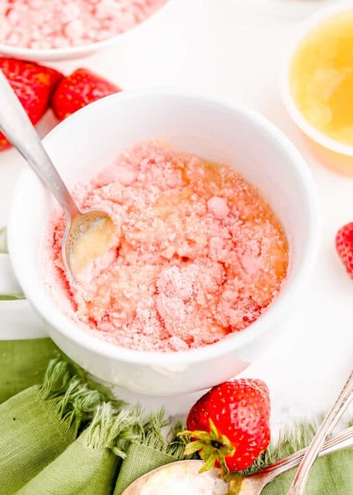 a metal spoon mixes together strawberry cake mix and applesauce in a white mug