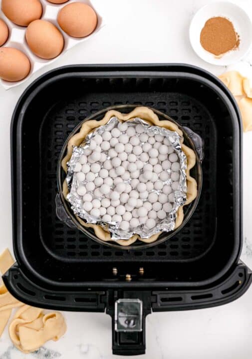 pie crust with tin foil and pie weights in the basket of an air fryer