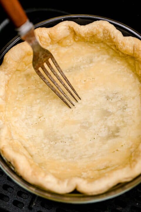 a fork pierces the baked pie crust