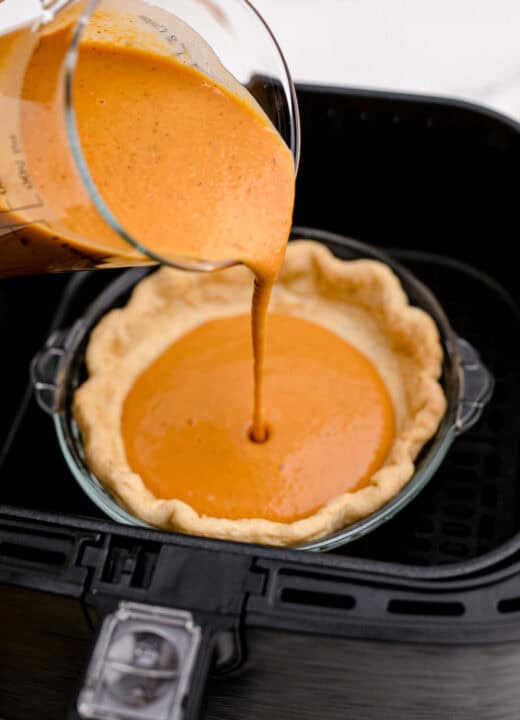 pouring pumpkin pie filling into a pie crust in the air fryer