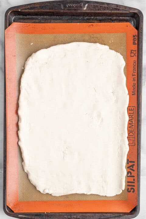 pizza dough pressed out into a rectangle on a silicone baking mat