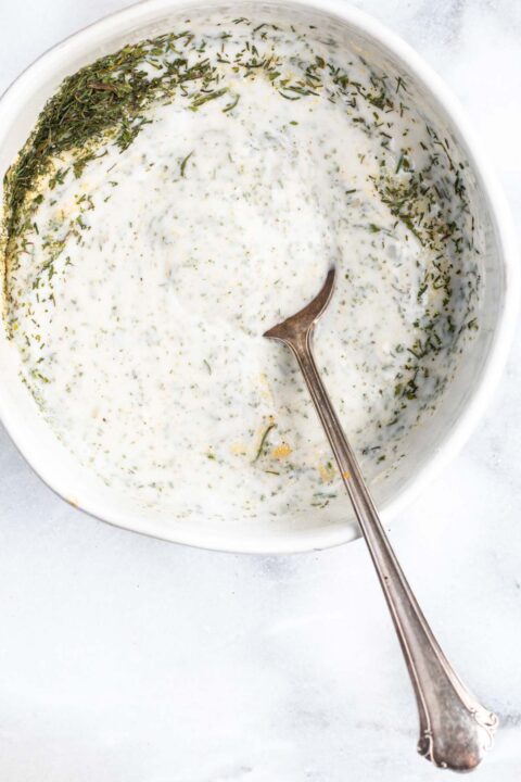 a metal spoon in a white dish mixing together ingredients for ranch dressing