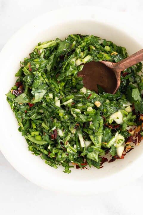 a mixture of herbs being mixed together with a wooden spoon in a white bowl