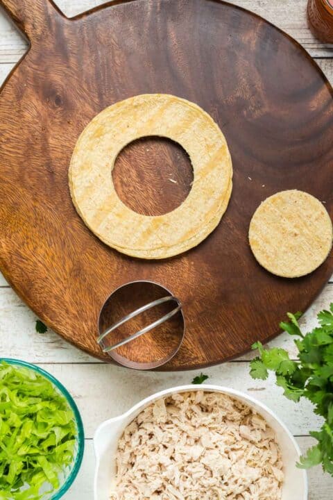 a 3” biscuit cutter cut a circle in the corn tortilla on a wooden cutting board
