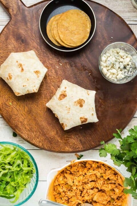 the buffalo chicken crunchwrap is seam-side down on the wooden cutting board