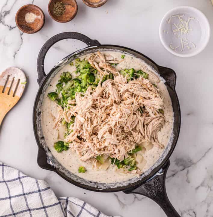 broccoli, potatoes, and shredded chicken added to alfredo pot pie mixture in a cast iron skillet