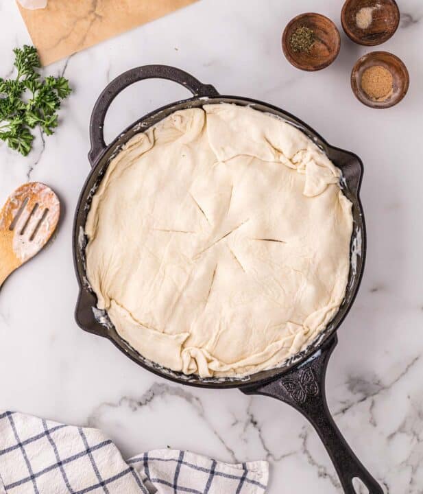 puff pastry added on top of alfredo pot pie mixture in a cast iron skillet with slits in the top of the puff pastry