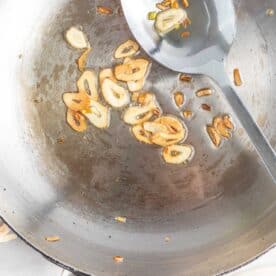 browned garlic slices in a metal skillet with a metal spoon