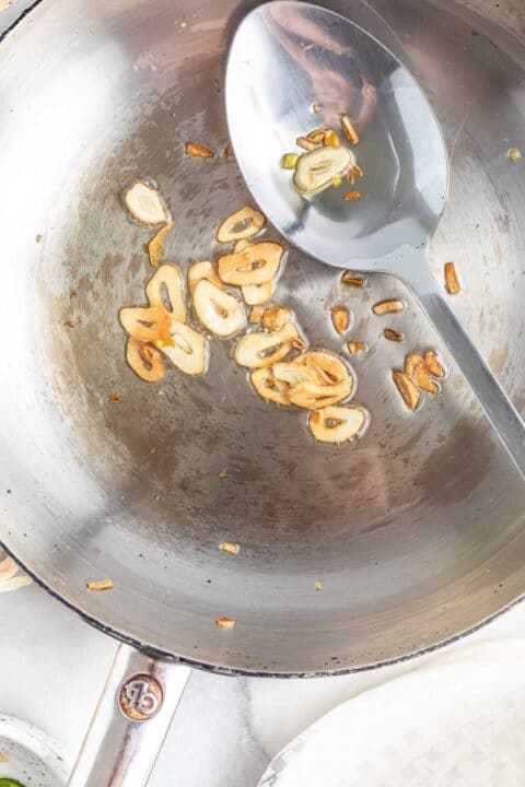 browned garlic slices in a metal skillet with a metal spoon