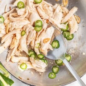 serrano peppers, shredded chicken, and browned garlic slices in a metal skillet with a metal spoon