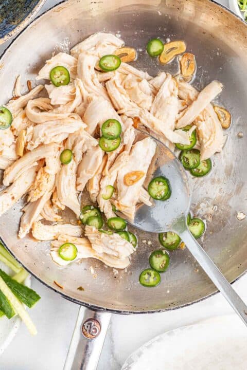 serrano peppers, shredded chicken, and browned garlic slices in a metal skillet with a metal spoon