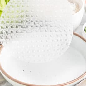 rice paper being dipped into a shallow bowl of water
