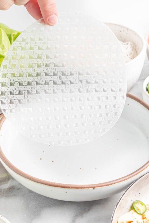 rice paper being dipped into a shallow bowl of water