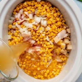 corn kernels, onion, bacon, and potatoes in the insert of a slow cooker with chicken broth being poured in