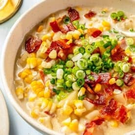 a bowl of corn chowder in a speckled bowl topped with fresh green onions and chopped bacon
