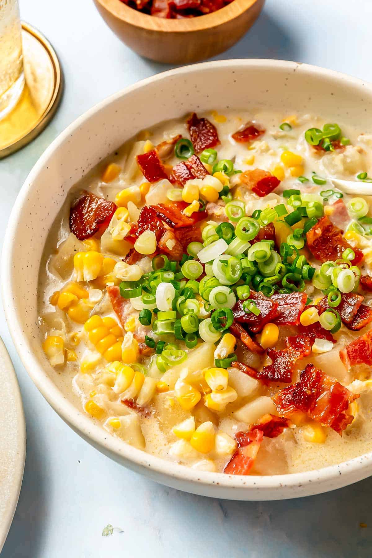 a bowl of corn chowder in a speckled bowl topped with fresh green onions and chopped bacon