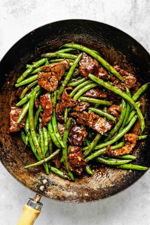 green beans and flank steak covered in soy sauce mixture in a wok