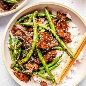 a pink bowl of green bean beef stir fry with white rice and wooden chopsticks