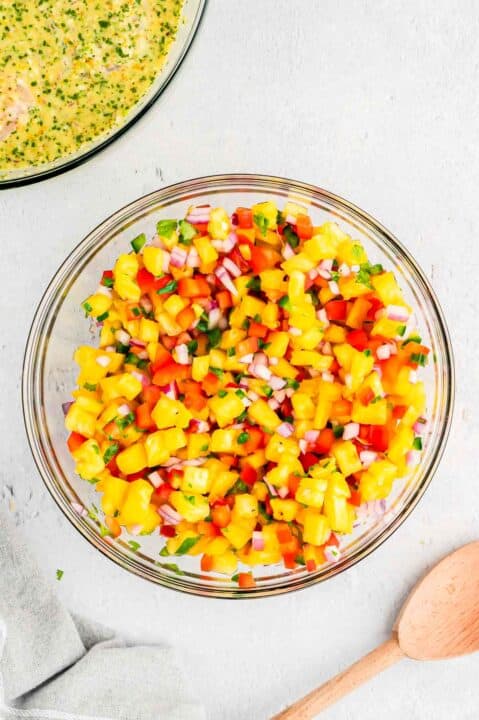 pineapple salsa in a clear bowl next to a wooden spoon