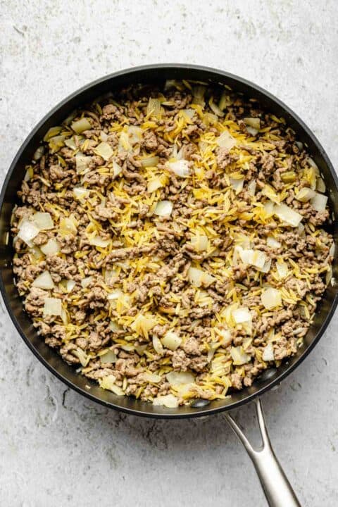 uncooked orzo pasta is added to a nonstick skillet with ground beef and onions