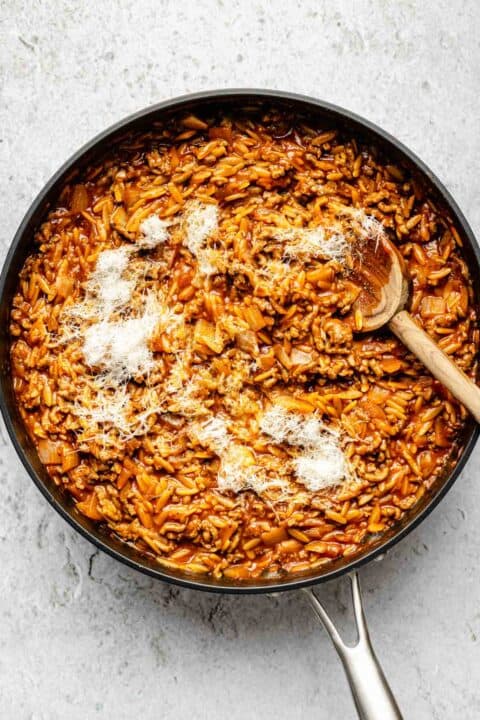 parmesan cheese sprinkled on top of cooked ground beef and orzo in a nonstick skillet with a wooden spoon