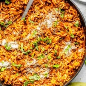 ground beef and orzo in a large nonstick skillet garnished with fresh basil leaves and grated parmesan cheese with a metal spoon