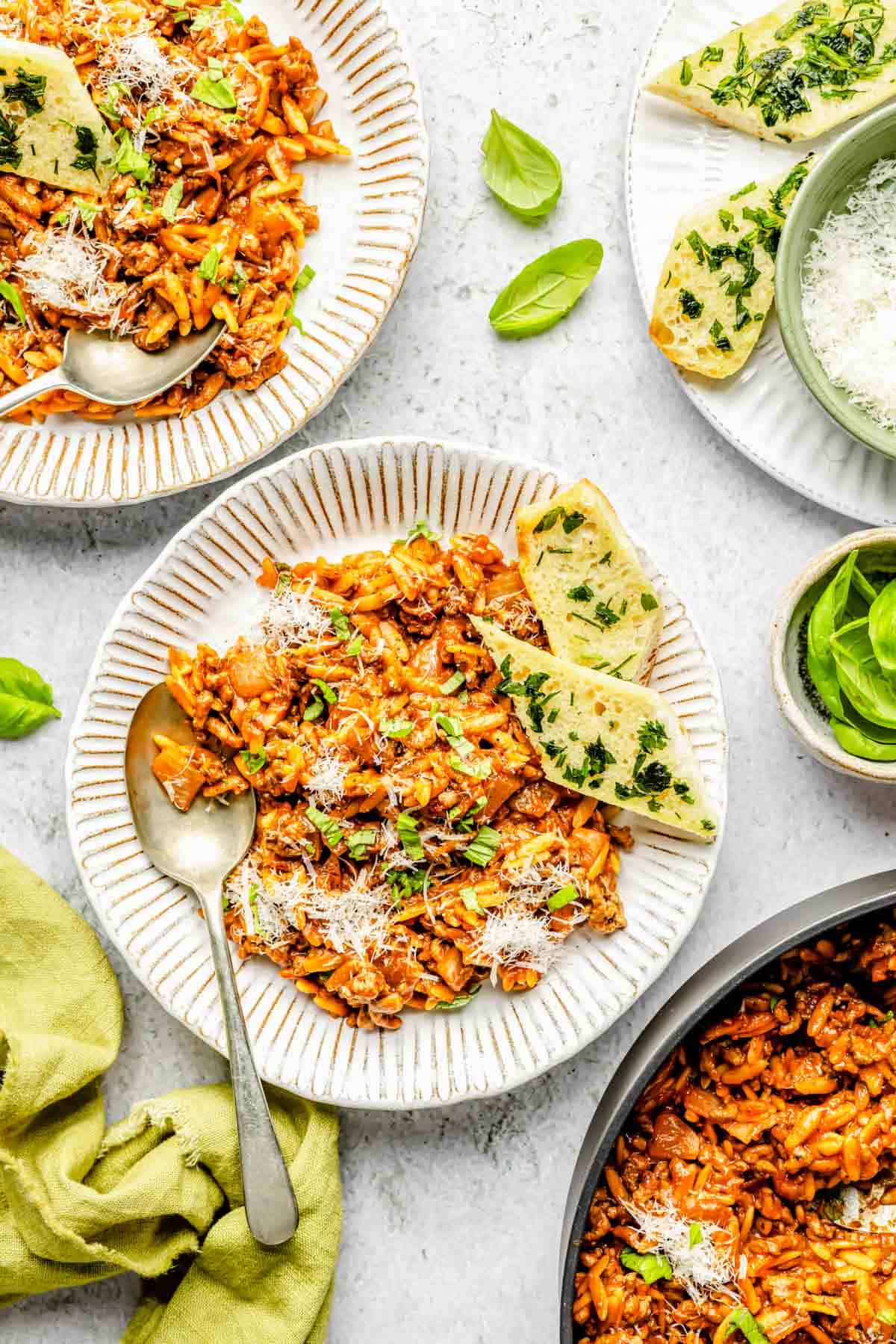 ground beef and orzo on plates next to garlic bread and a metal spoon