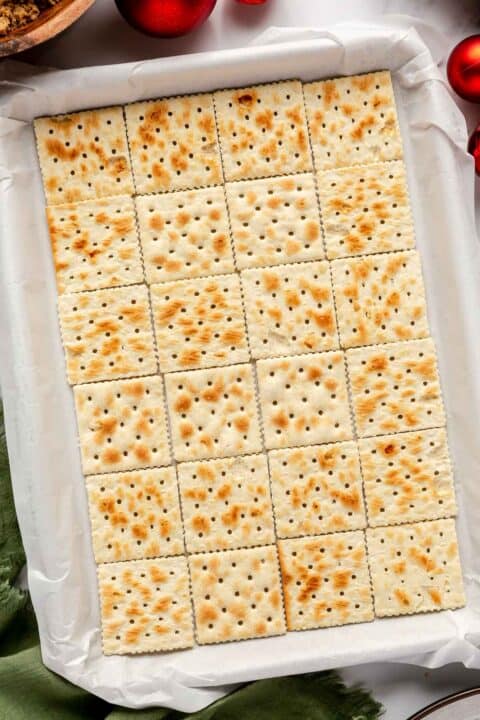 saltine crackers on a parchment paper lined metal baking sheet
