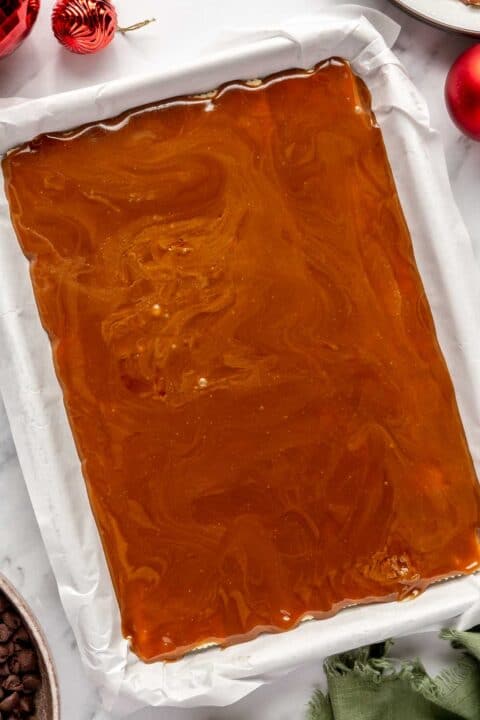 melted butter and brown sugar mixture is poured on top of the saltines in the baking sheet