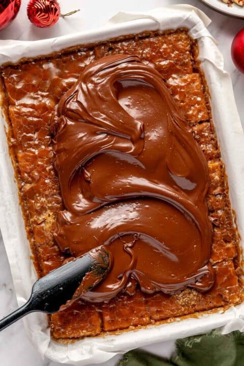 chocolate is being spread on top of cooled butter and brown sugar mixture