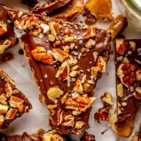 a triangular shaped saltine toffee piece has chopped pecans and sea salt sprinkled on top