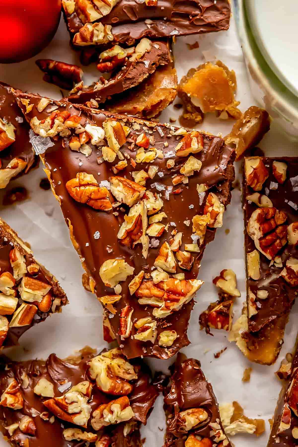 a triangular shaped saltine toffee piece has chopped pecans and sea salt sprinkled on top