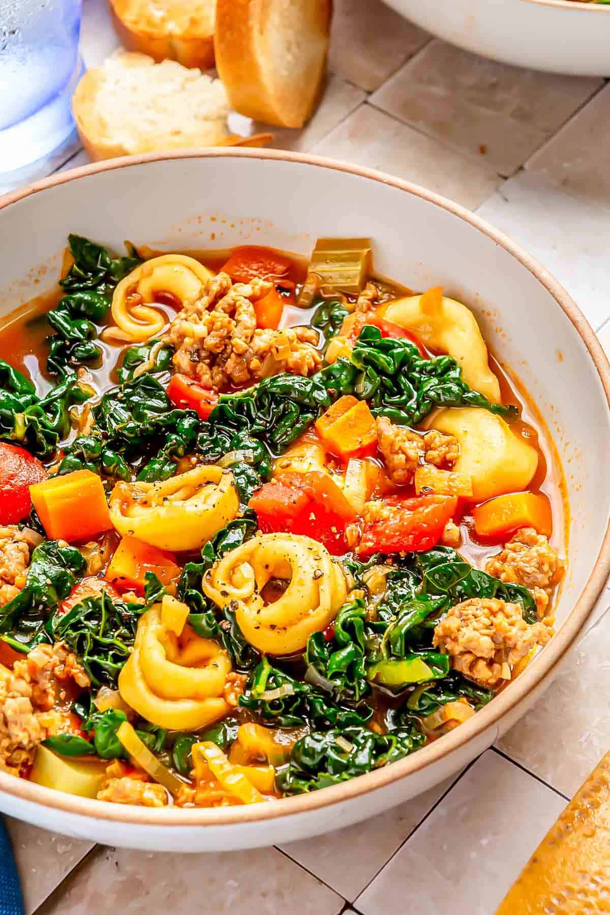 sausage tortellini soup in a bowl with freshly cracked black pepper on top