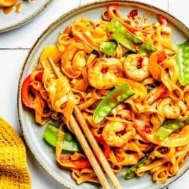 shrimp noodle stir fry on a plate with chopsticks holding twirled rice noodles