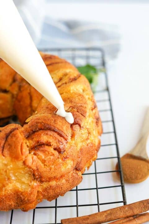 cream cheese glaze is being piped onto apple monkey bread