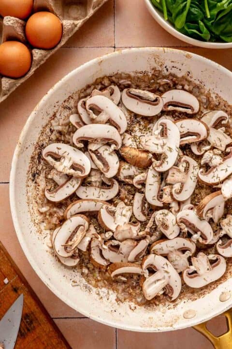 sliced mushrooms and thyme added to the shallots in the skillet with bacon grease
