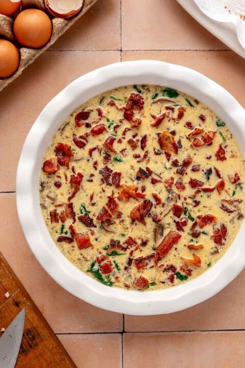 bacon pieces sprinkled on top of egg mixture in a baking dish