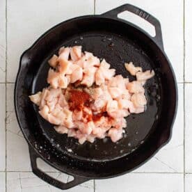 cubed chicken and seasonings in a cast iron skillet