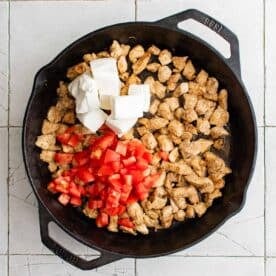 tomatoes, cream cheese, and cooked chicken in a cast iron skillet