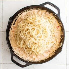 cooked spaghetti has been added to a cast iron skillet