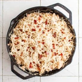 mozzarella cheese and more bacon is topped on chicken spaghetti in a cast iron skillet