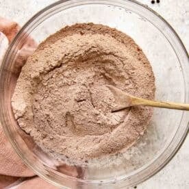 flour, cocoa powder, and other dry ingredients in a clear bowl and wooden spoon
