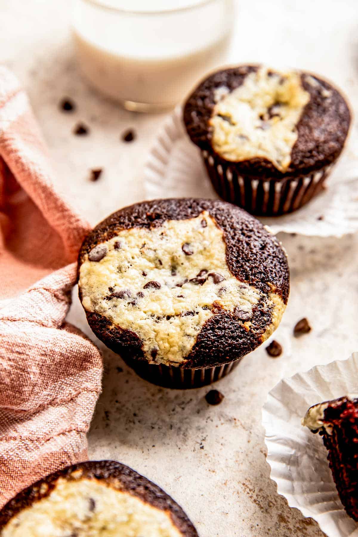 a chocolate cream cheese muffin is on a grey surface next to another cupcake