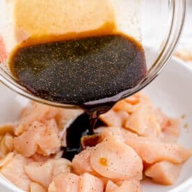soy sauce mixture is being poured on cubed raw chicken in a white bowl
